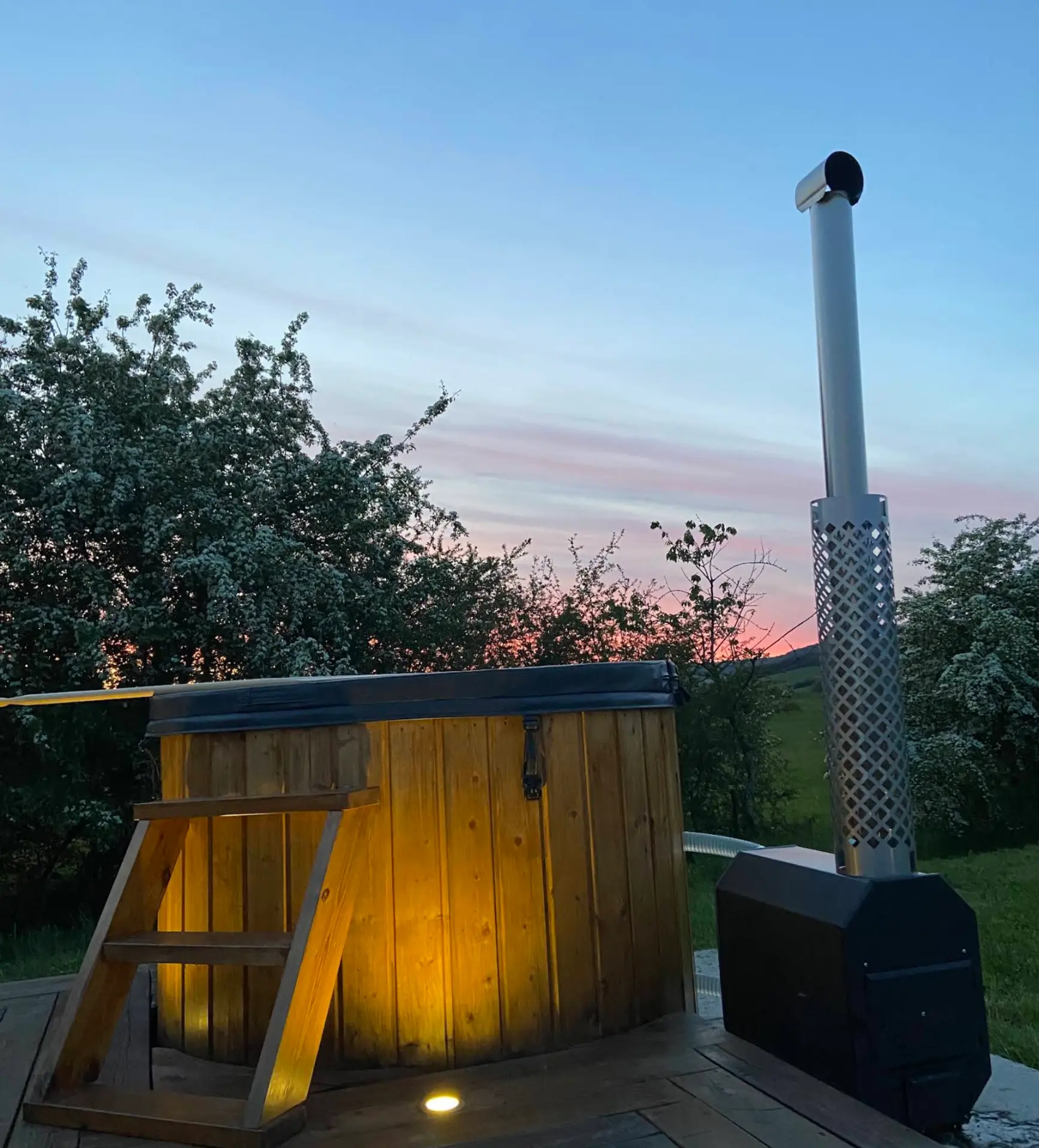 Bain nordique en bois chauffé au feu de bois sur la terrasse, éclairé au coucher du soleil