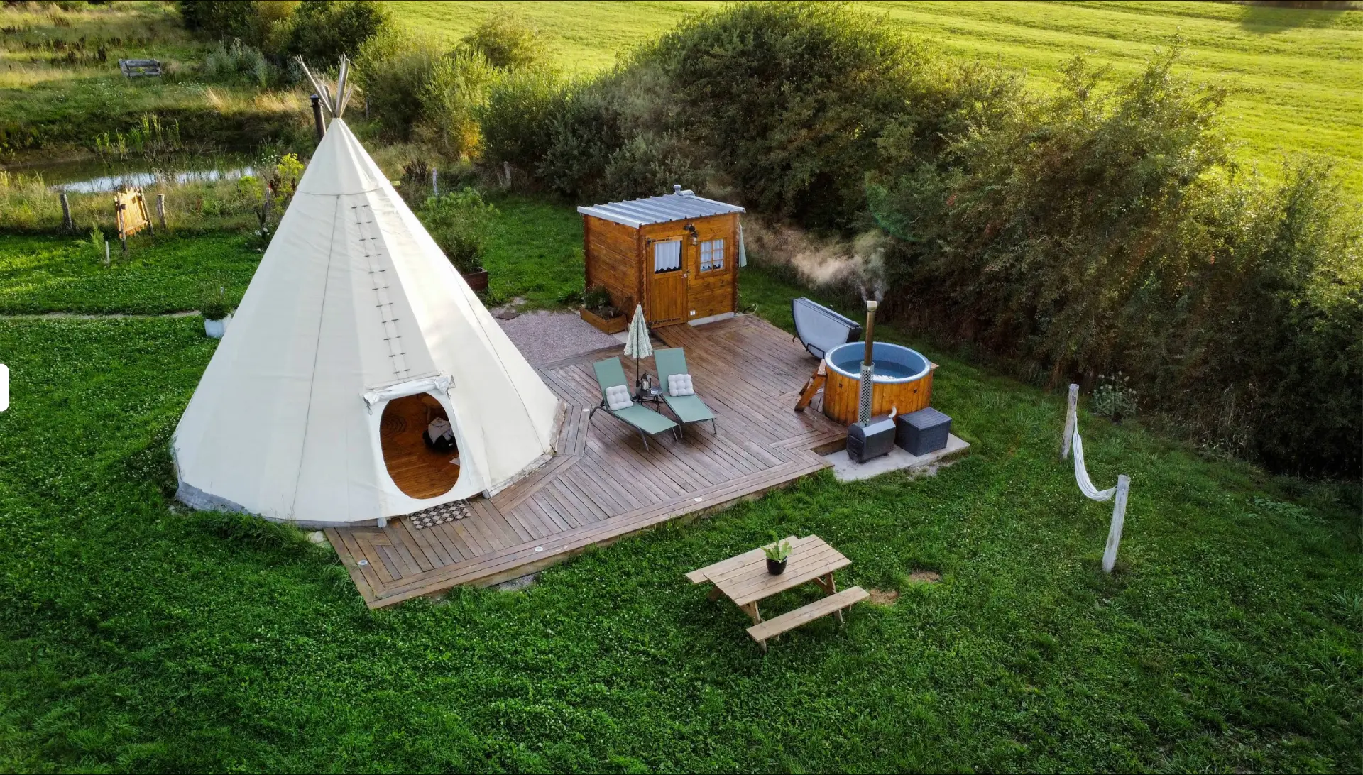 Vue aérienne du tipi, de la terrasse en bois, du chalet sanitaire et du bain nordique fumant