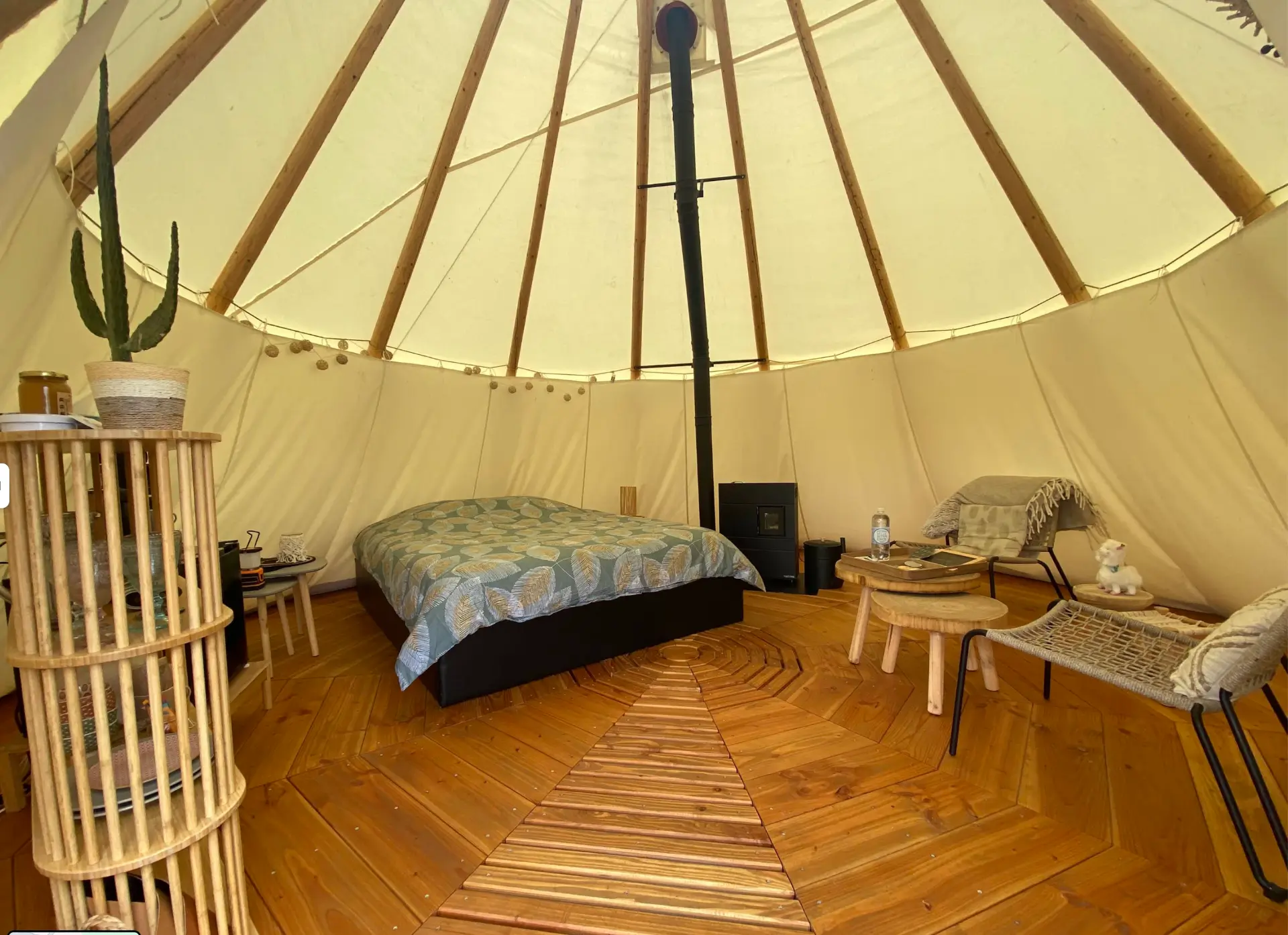 Intérieur du tipi avec lit double, poêle à bois et parquet en bois disposé en étoile